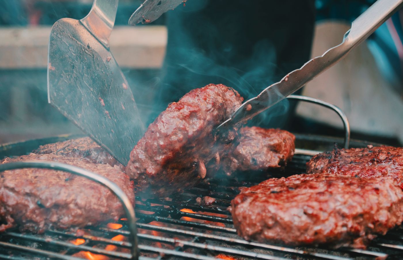 Burgers being turned on a smoky grill